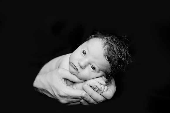 stunning black and white image of a newborn baby boy in daddy's hands at tanis saucier photography in her Montreal studio