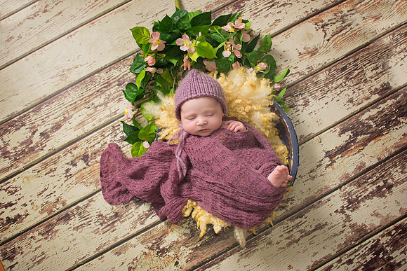 sweet image of a newborn baby girl wrapped in a lilac knit wrap posed in a wooden bowl with flowers surrounding her at tanis saucier photography in her Montreal studio